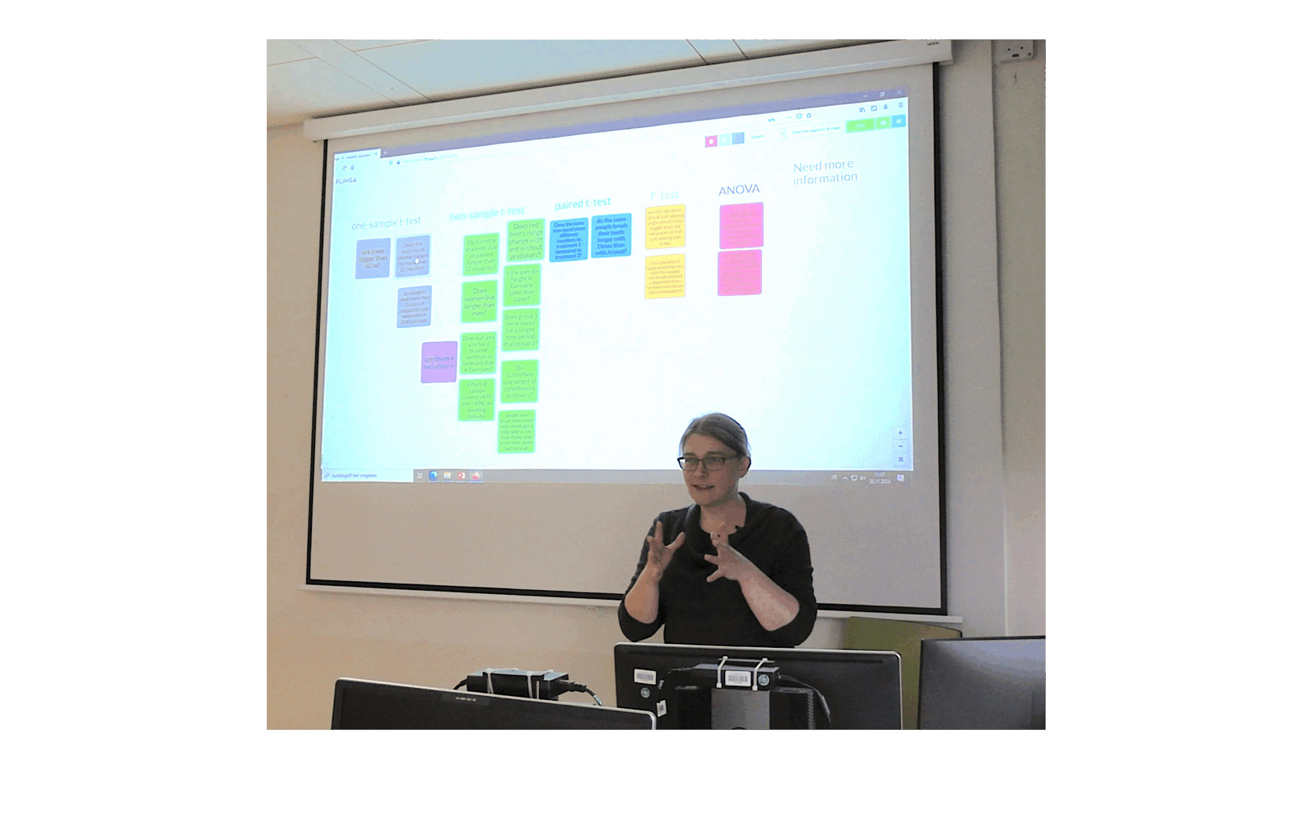 „Katrin steht vor der Projektion des Whiteboards und erklärt die Inhalte mit Gesten.“